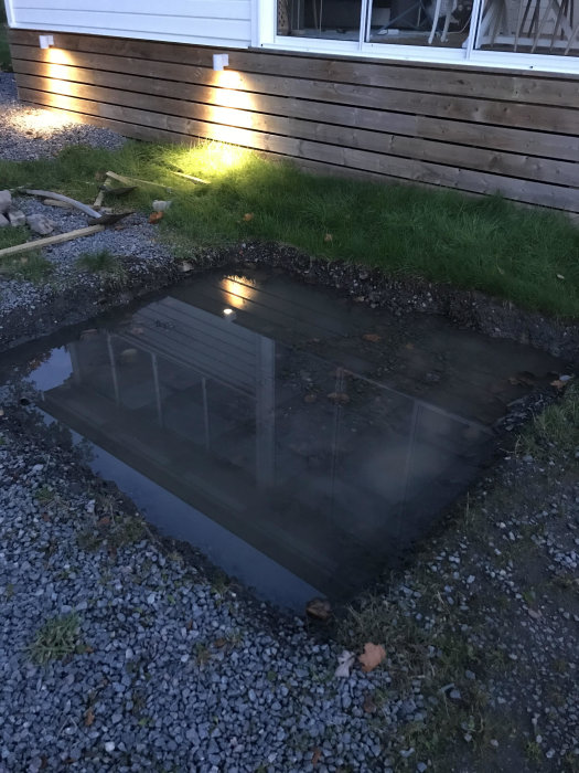 Vattenfylld utgrävning för spabad nära ett uterum, med stående vatten på lera.