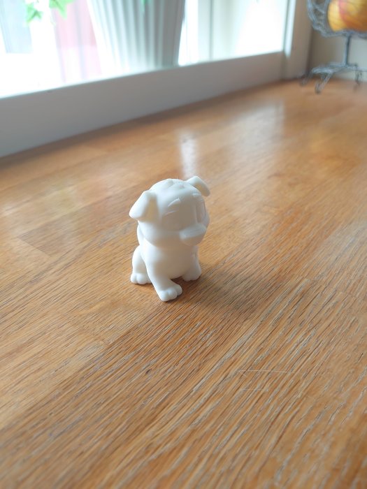 3D-utskriven vit hundfigur på trägolv med suddig bakgrund.