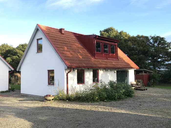 Ett nyrenoverat hus med rött tak och nyputsad vit fasad omgivet av grönska.