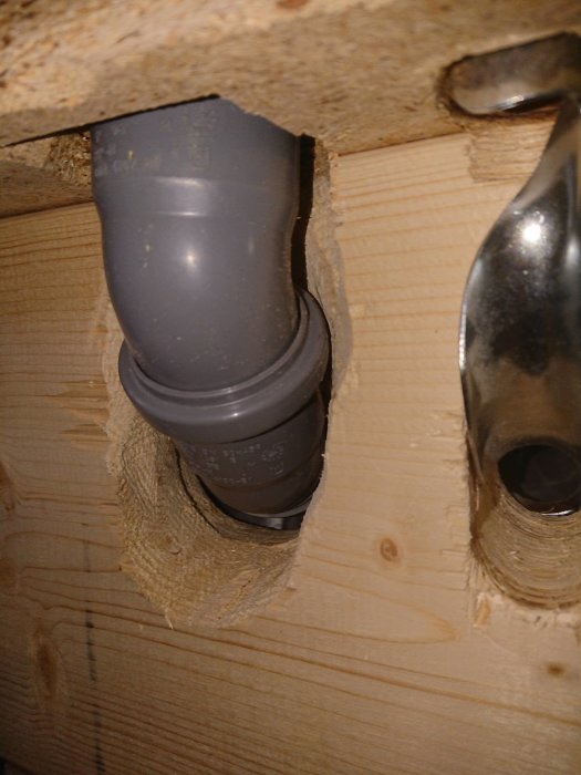 Avloppsrör som går genom utskuren öppning i en trägolvregel under badrumsrenovering.