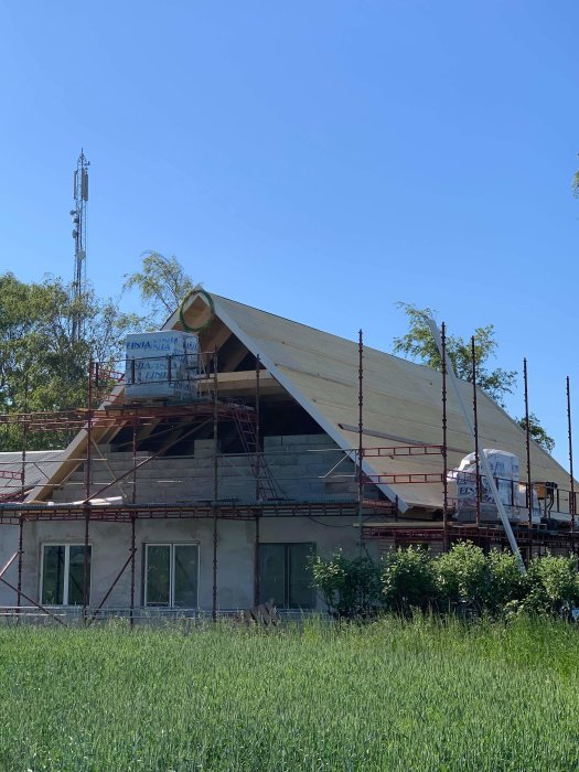 Renoverad fastighet med nya takstolar och borttaget tak under klarblå himmel, omgiven av byggnadsställningar.