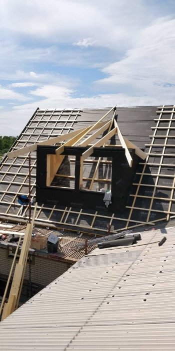 Delvis renoverat tak med nya takstolar och svart vindskyddsfolie på en byggnad under klar himmel.