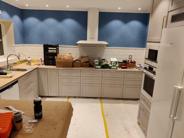 Kök under renovering med vita skåp, kakelvägg, och verktyg på laminatbänk.