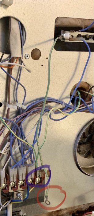Öppen elektrisk kopplingsdosa med en jordkabel markerad i röd ring kopplad till jordanslutning markering i lila.