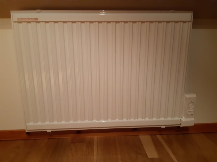 Nyinstallerat vitt elektriskt element på vägg med synliga kabeluttag på höger sida.