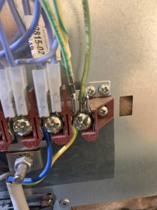 Gulgrön jordkabel ansluten till höger sida av en metallklemrad i en elektrisk installation.