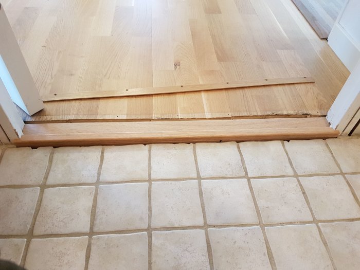 Närbild av ekkantströskel mellan trägolv och kakelplattor vid badrummet.