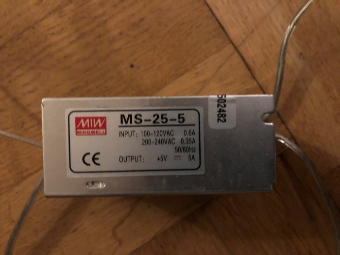 En Mean Well MS-25-5 strömförsörjningsenhet på trägolv med synliga specifikationsetiketter.