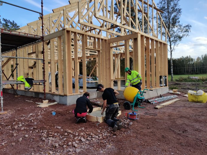 Personer arbetar på en byggarbetsplats med trästomme för ett hus och gjutning av fundament.