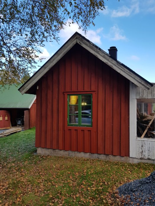 Röd stuga med nyinstallerat fönster och färdigställd panel, fönsterbleck syns, omgiven av natur.