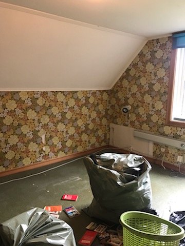 Sovrum före renovering med gammalt blommigt tapet och oordning på golvet.