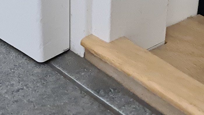 Tröskel i trä som inte ligger i linje med dörrens vita karm, synligt högre än golvet.