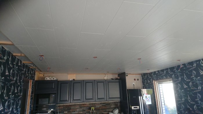 Nytt grått innertak i ett kök med mörka skåp och ledningar hängande ner.