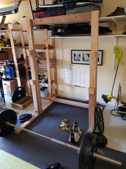 Hemmagjord squat rack av trä i ett garage med skivstång och vikter på golvet.