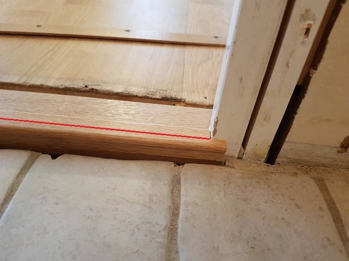 Tröskel av trä markerad med röd linje vid övergång från trägolv till klinker.