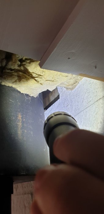 Vattenläckage vid rökrör och isolering bakom en kamin, synlig genom en ficklampa.