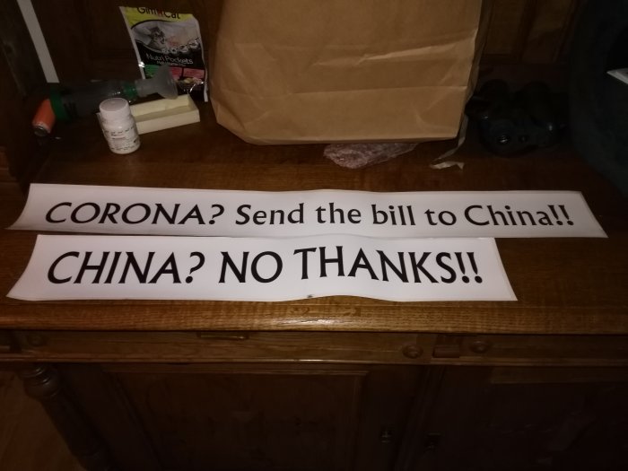 Två klistermärken med texten "CORONA? Send the bill to China!!" och "CHINA? NO THANKS!!" på ett bord.