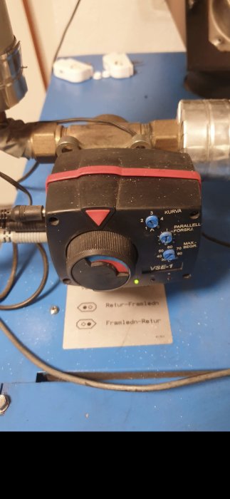 Shuntventil placerad på ett blått underlag med inställningsknappar och anslutna kablar.