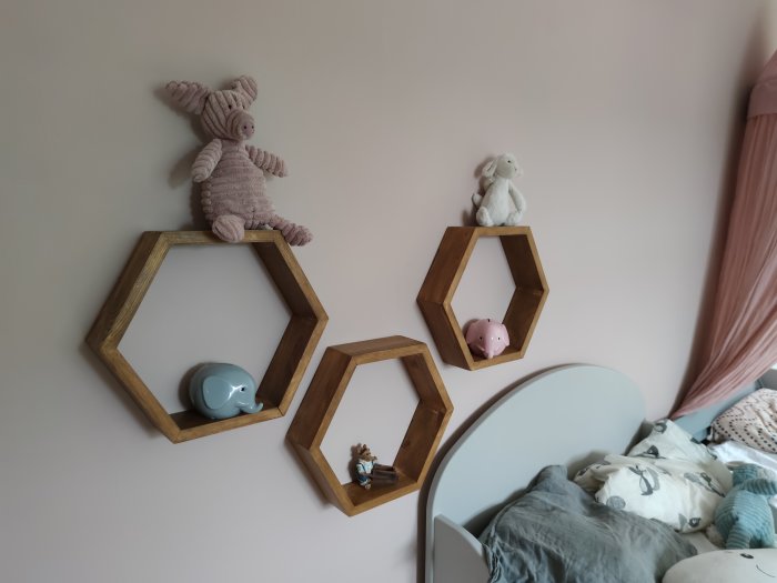 Hexagonala trähyllor på en vägg med leksaker och prydnadsföremål i barnrum.