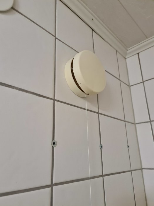 Tilluftsventil på en kaklad vägg med synliga installationskablar och en vit takkant.