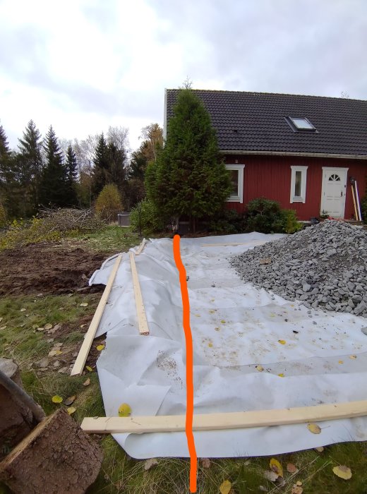 Fotografi av gräsmark och grus vid hus, med orange linje markerande planerad rörgrav.