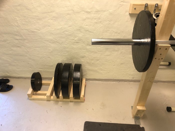 Hemmagym med självgjutna viktskivor på träställ och 20 kg stång vid limträpelare.