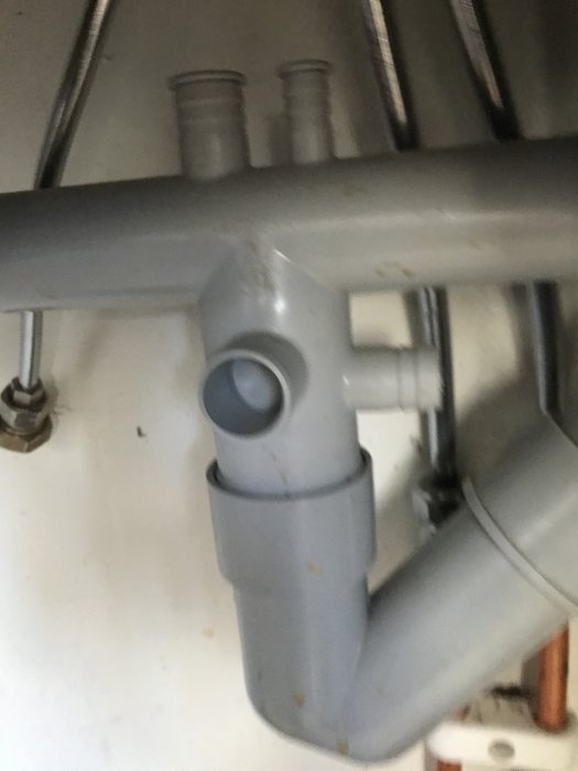 Suddig bild av undersidan av ett kökshandfat med avloppsrör och anslutningar.
