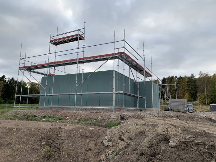 Hus under uppförande med ställningar på byggarbetsplats under en molnig himmel.