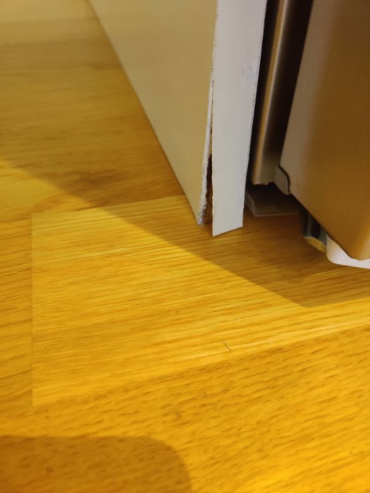 Vit dörrkarm med skavanker står mot ett trägolv med svagt ljus.