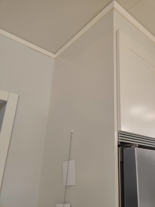 Vit vägg och tak med lister i ett kök, dåligt ljus, bredvid ett kylskåp.