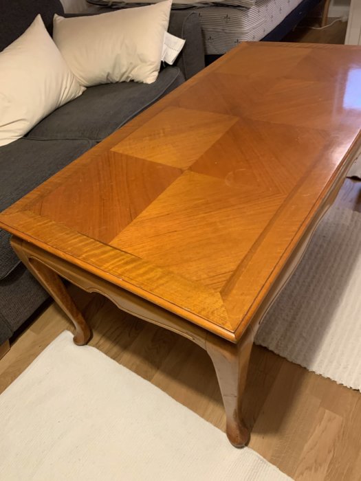 Ett brunfärgat träbord med lackad yta, redo för målning, i ett vardagsrumsmiljö.