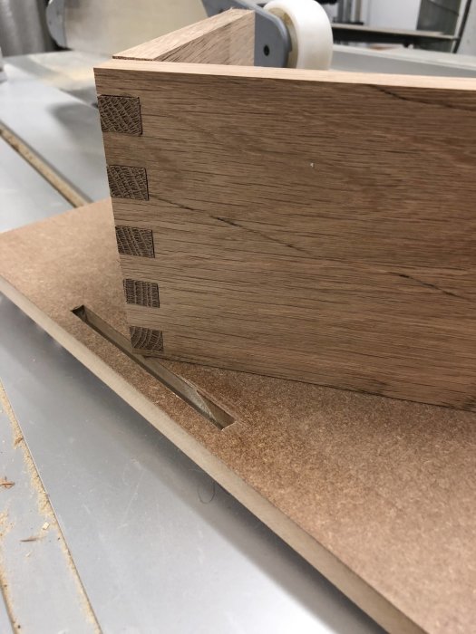 Närbild på ett trästycke med laxstjärtssammanfogningar i en vertikalfräs, visa upp experimentell prototyp för tappning.