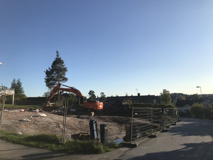 Grävmaskin på en bergig tomt med avspärrning och stora stenbumlingar under en klarblå himmel.