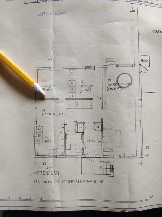Planritning av ett hus med markerad vägg som ska tas bort, med en penna som pekar på den aktuella väggen.