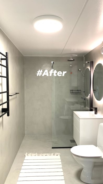 Renoverat badrum med microcement på väggar och golv, duschhörna med glasvägg, toalett och svart handdukstork.
