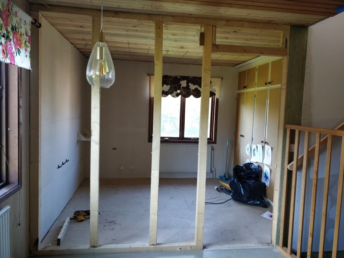 Rum under renovering med synliga reglar och en takbjälke där en vägg planeras att tas bort.