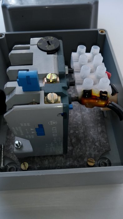 En öppen elektrisk låda med en motorskyddsbrytare inställd mellan 16-25A och anslutna hjälpkontakter, viss varmgång synlig.