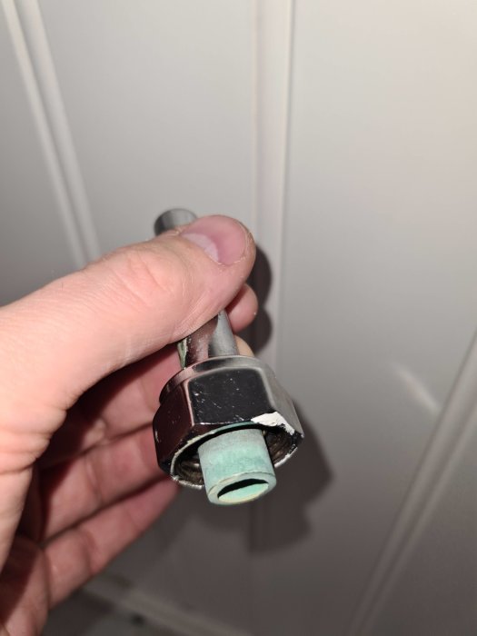 Hand håller en vattenrörskoppling med en klämring och gummipackning synliga vid anslutning av ett vitt rör.