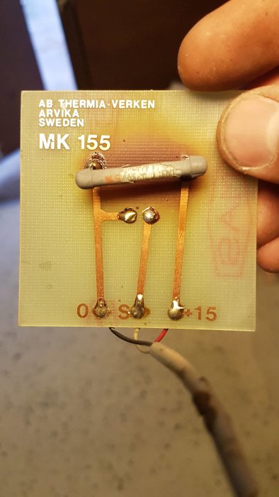 Hand som håller ett gammalt elektronikkort från AB Thermia-Verken med texten "MK 155", kopparbanor och komponenter synliga.