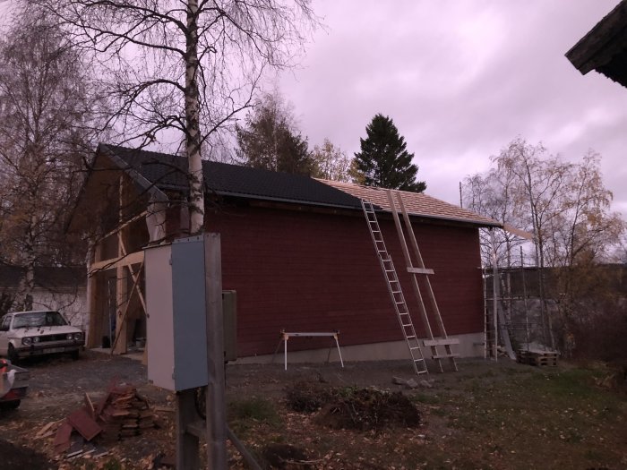 En röd byggnad under konstruktion med färdigt tak på en sida och pågående arbete på den andra. Stegar lutade mot byggnaden.