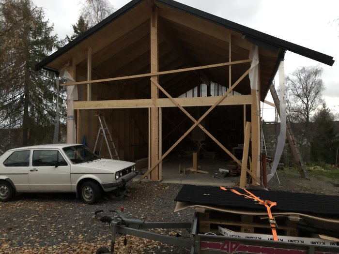 Halvfärdigt bygge av ett garage med taket delvis pålagt och byggmaterial i förgrunden.