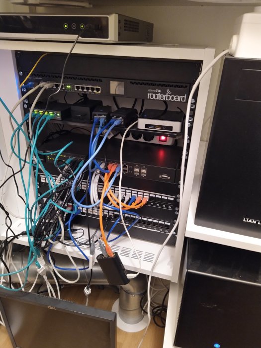 Oorganiserad nätverksskrubb med trassliga kablar, patchpaneler, en PoE-switch och UPS.