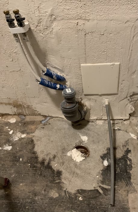 Ett ofärdigt golv i ett renoveringsprojekt med ett synligt hål, rörinstallationer, och en del kablar.