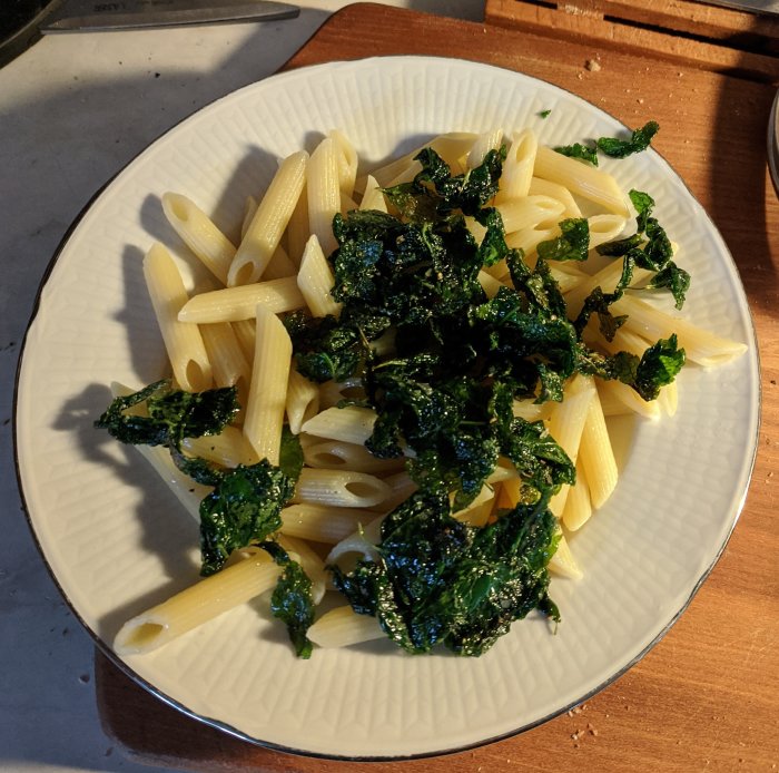 Pasta med brynta kirskålsblad på en vit tallrik.