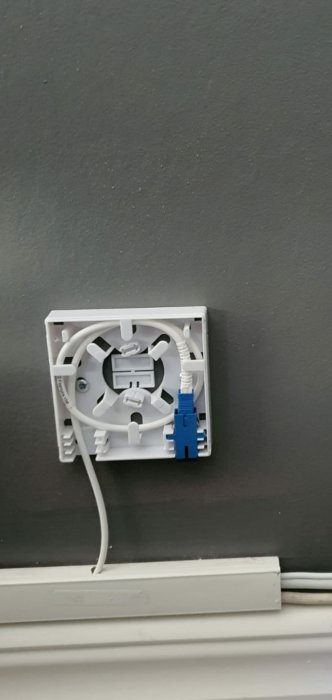 En vit kopplingsbox för fiberkabel på mörk vägg med en ansluten fiberkabel.