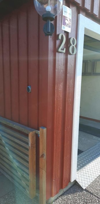 Röd garageport med siffrorna 28, en kodlåspanel till vänster och en utomhuslampa överst.