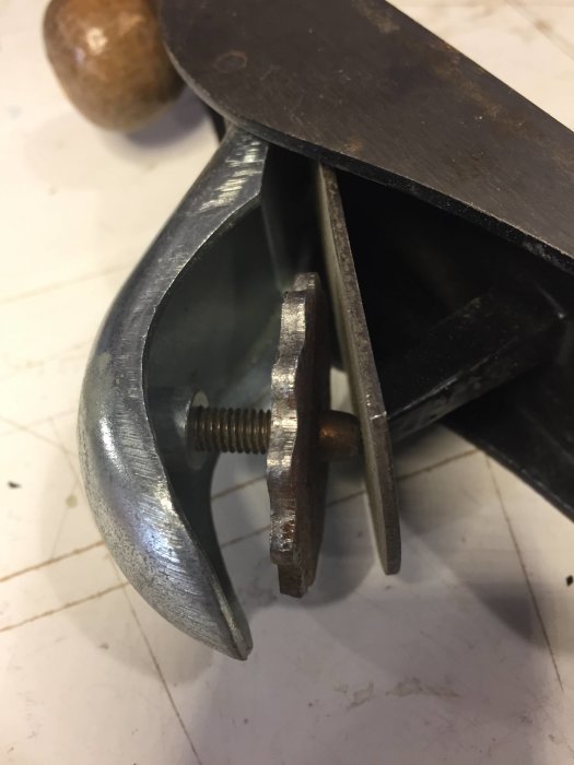 Närbild på en gammal handhyvel som visar justerskruven och skäret mot en suddig bakgrund.