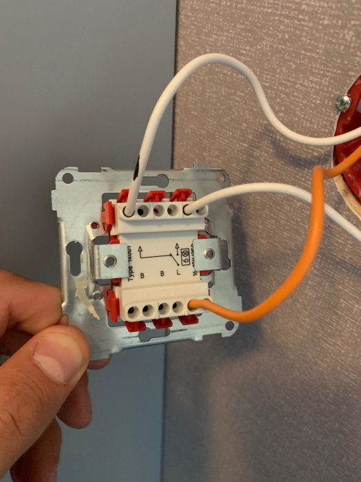 Öppen strömbrytare i vägg med tre kablar, två vita och en orange, vid en installationsprocess.