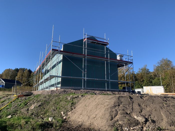 Hus under konstruktion med ställning och presenningar vid en klarblå himmel.