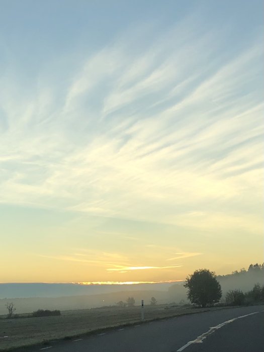 Soluppgång och strimmiga moln över en landsväg påväg till jobbet.